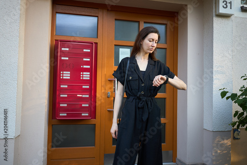 Woman checking her watch while standing by a red mailbox and wooden door