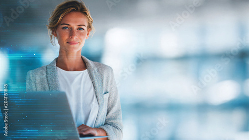 Confident businesswoman standing with laptop in modern bright office representing leadership corporate success and data analytics