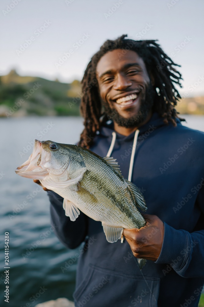 Obraz premium Man proudly showing largemouth bass on lakeside pier
