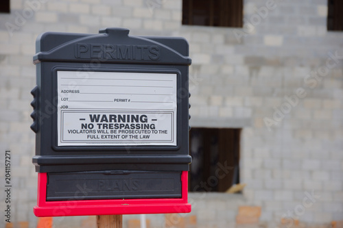 Photos Permit box and prominent no trespassing sign on a residential construction site in front of a partially built cinderblock house, conveying safety, regulation and work-in-progress on a cloudy day