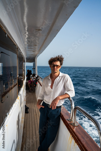 Epic luxury yacht cruise man portrait vertical linen shirt lifestyle ocean background.
