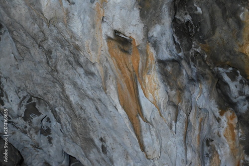 Abstract cave wall formation with orange mineral drapery and tehtured limestone rock.