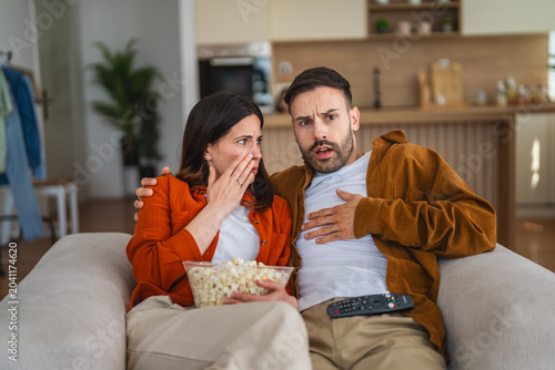 Foto Couple watching thrilling movie at home holding popcorn