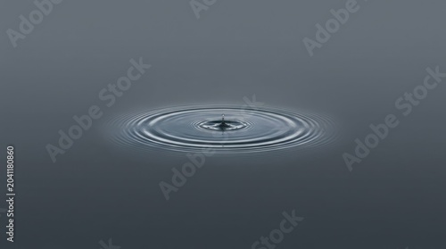 A single water drop creates perfect ripples on a calm, dark surface.