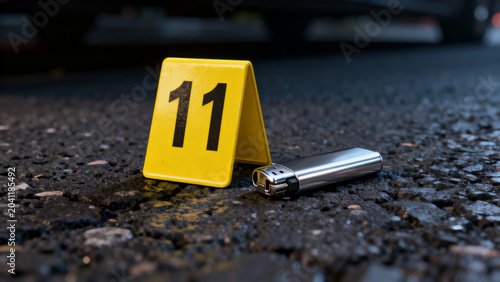 Crime scene evidence marker beside metallic lighter on asphalt