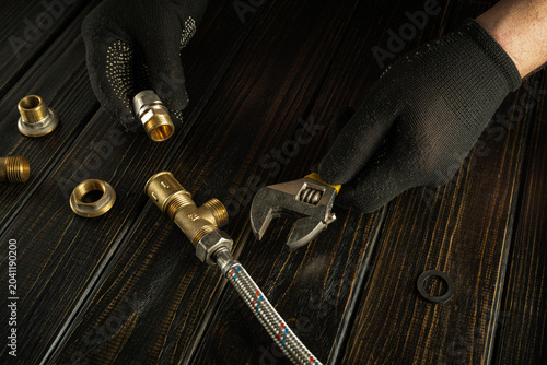 Fotografie In a home setting, a person wears black gloves and uses a wrench on a plumbing part
