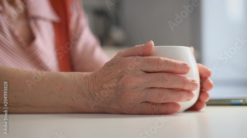 An elderly woman warms her hands on a cup of tea, close-up. Deterioration of blood flow in old age concept