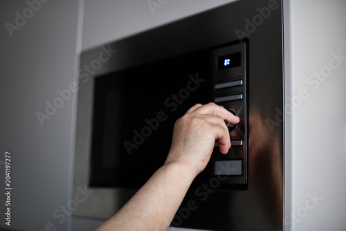 Photos Close-up of a person's hand adjusting settings on a modern built-in microwave oven