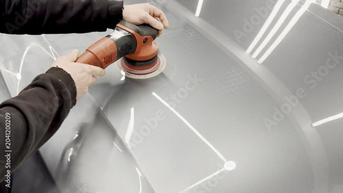 A car service worker polishes the car body with a polishing machine. Detailing and polishing of the car. Car detailing - hands with an orbital polishing machine in an auto repair shop. PDR. 