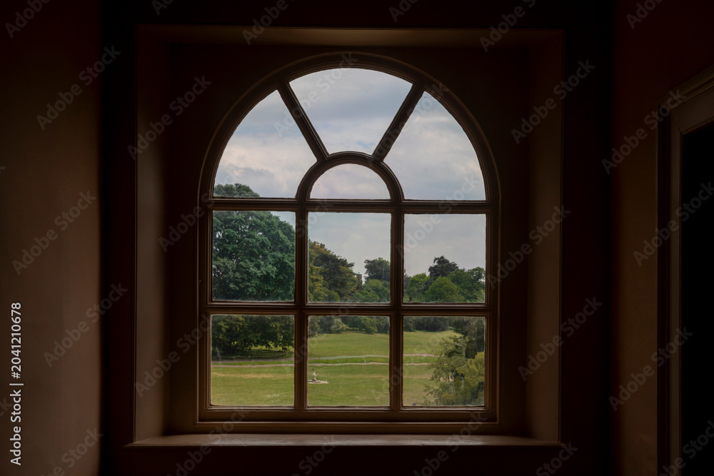 Fototapeta premium A symmetrical shot of a classic arched glass window looking out onto a wide green lawn. 