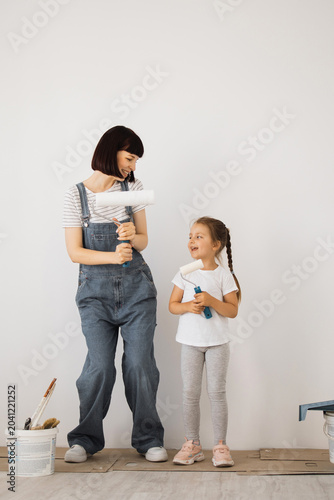 Tableau sur toile A mother and her young daughter stand side-by-side, holding paint rollers and sm