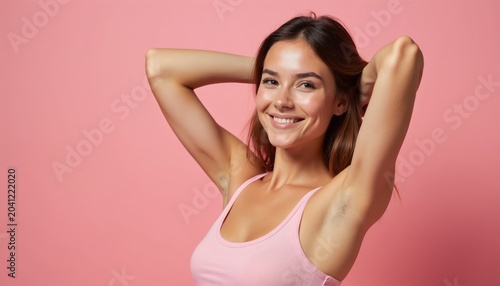 Smiling young woman in pink top has arms raised showing smooth skin. Healthy female model displays clean underarms after hair removal. Natural beauty.