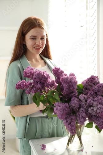 Teenage girl putting lilac flowers into vase at home