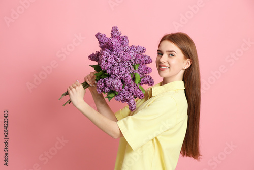 Teenage girl with bouquet of lilac flowers on pink background