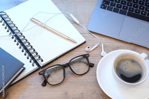 Pair of stylish glasses, laptop, notepad, earphones and cup of coffee on wooden table, above view
