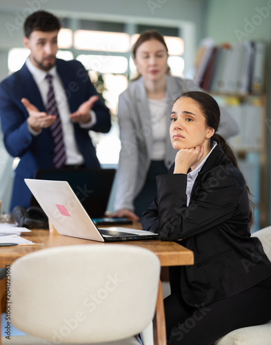Group of women and man scold young woman while she sits looking sad in office