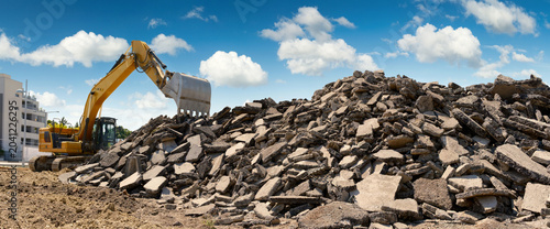 Photos A yellow excavator piling rubble on a construction site, with nice blue sky, pan