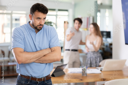 Foto Upset young man feeling excluded while other colleagues gossiping behind his bac