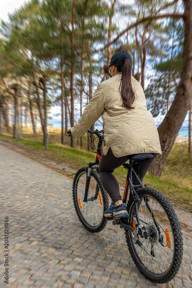 Fototapeta premium Woman cycling on forest path. Active seaside recreation scene
