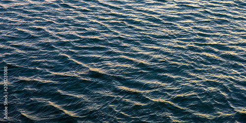 Dark sea water with golden sparks. Textured ocean waves background.