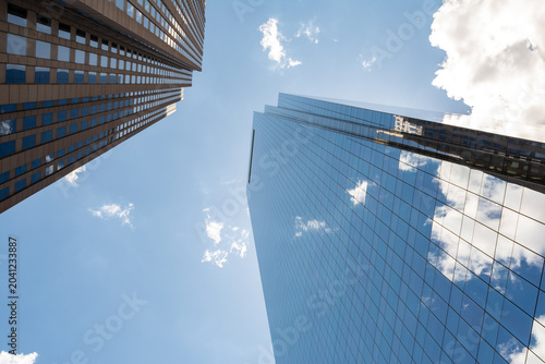Looking up at modern glass skyscrapers in Philadelphia, Pennsylvania with reflections of clouds and blue sky.
