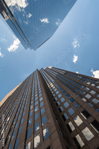 Looking up at modern glass skyscrapers in Philadelphia, Pennsylvania with reflections of clouds and blue sky.