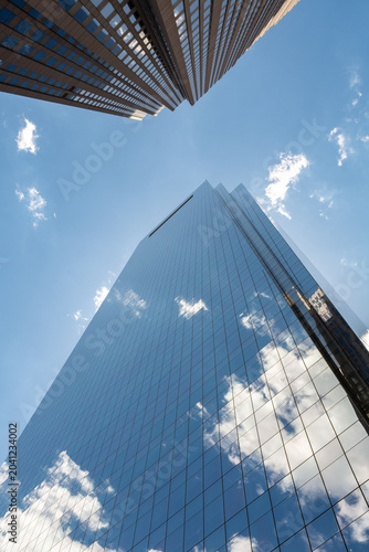 Looking up at modern glass skyscrapers in Philadelphia, Pennsylvania with reflections of clouds and blue sky.
