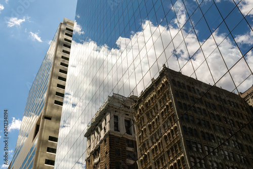 Looking up at modern glass skyscrapers in Philadelphia, Pennsylvania with reflections of clouds and blue sky.