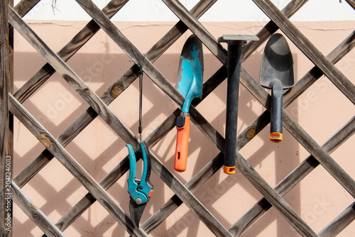Garden hand tools hanging on a planter trellis.