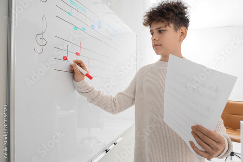 Teenage boy writing music notes on whiteboard in classroom