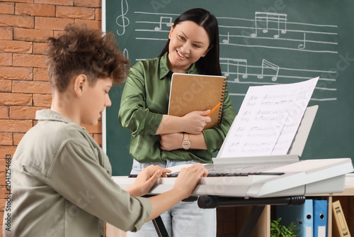 Teenage boy with teacher learning to play synthesizer in music class