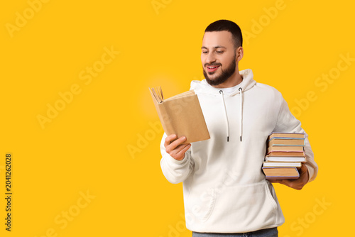 Bild auf Leinwand Young man with stack of books on yellow background