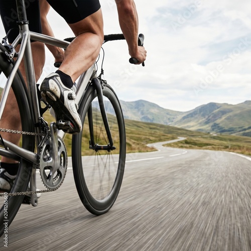 Close-up of a cyclist pedaling a road bike on a mountain route. High-speed motion blur with huge empty copy space on the right side. Perfect for sports banners and marathon ads.