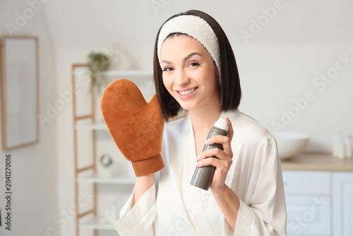 Konstfotografi Happy young woman with massage glove and bottle of self tanner mousse in bathroo