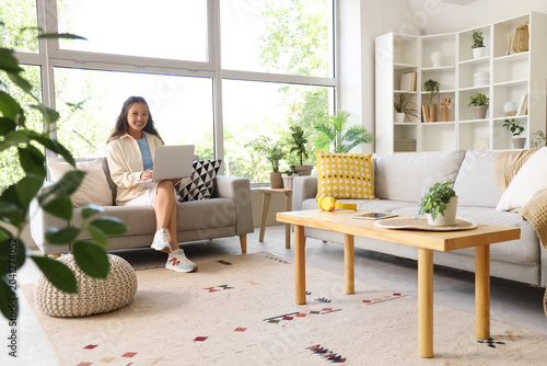 Young Asian woman using laptop on sofa at home