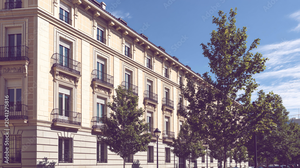 Obraz premium Classical apartment building facade behind trees on sunny street