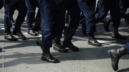 Close-up of uniformed personnel marching in synchronized formation along a paved street, black boots and blue trousers moving in rhythmic unison across double white lane markings.