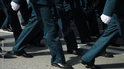Close-up view of uniformed personnel marching in synchronized formation during a formal parade, polished black shoes and dark trousers stepping in unison along asphalt roadway