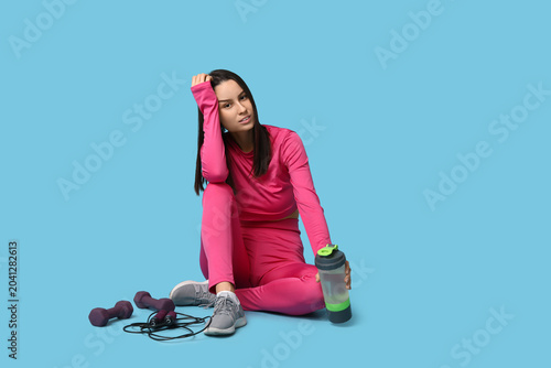 Young sporty woman with water bottle, skipping rope and dumbbells on blue bac...