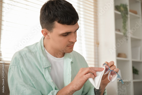 Handsome young man wiping eyeglasses at home