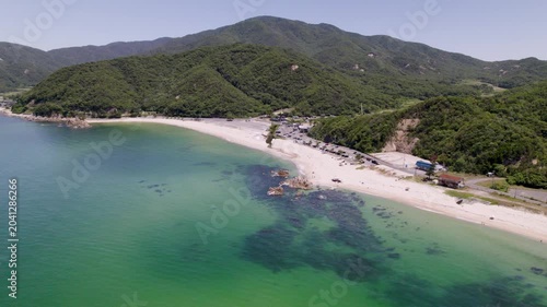斜め俯瞰・後退スライド】緑の山々と水晶浜海水浴場の美しい海岸線（ドローン映像）