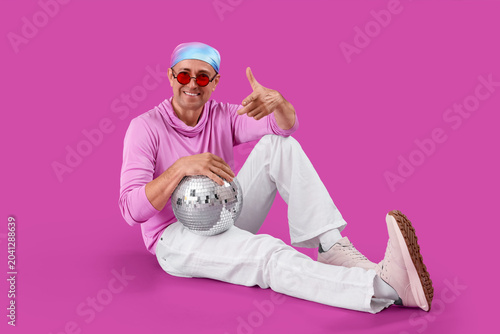 Cool mature man with disco ball sitting on purple background