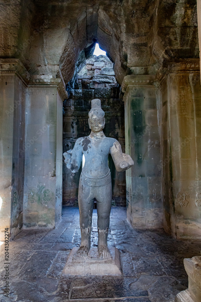 Fototapeta premium A stone statue of a deity stands within the ancient ruins of Angkor Wat, Siem Reap, Cambodia. The temple complex is a UNESCO World Heritage site.