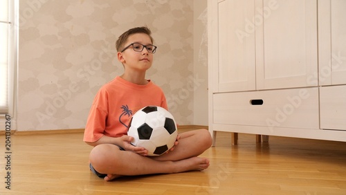 Foto Little boy wearing eyeglasses and an orange t shirt holding a soccer ball, sitti