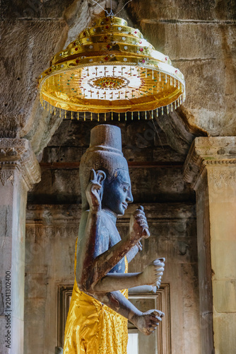 Cuadro en lienzo A stone statue of a multi-armed deity, draped in golden fabric, stands beneath a decorative umbrella inside a temple in Angkor Wat, Siem Reap, Cambodia