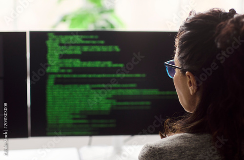 Woman programmer developer reading code on monitors. Back view in a tidy office  she analyzes syntax on a large screen  testing software and debugging code. Concept shows coding and focus.