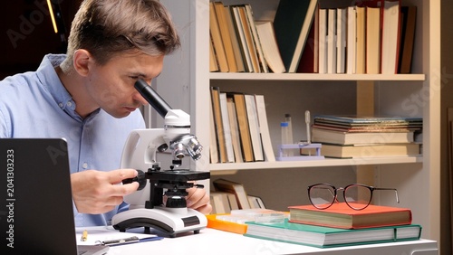 Slika na platnu Young man engrossed in scientific research, meticulously adjusting a microsope w