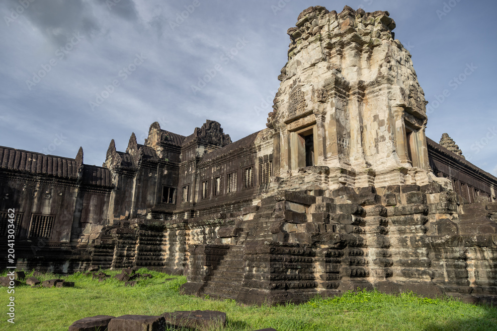 Fototapeta premium Angkor Wat temple complex in Siem Reap, Cambodia, showcases intricate Khmer architecture and bas-reliefs under a cloudy sky, a testament to ancient artistry.