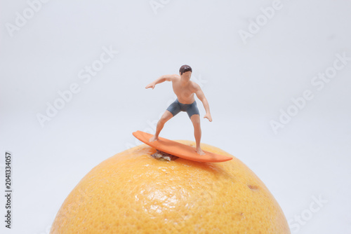 Miniature surfer riding fruit concept wave
