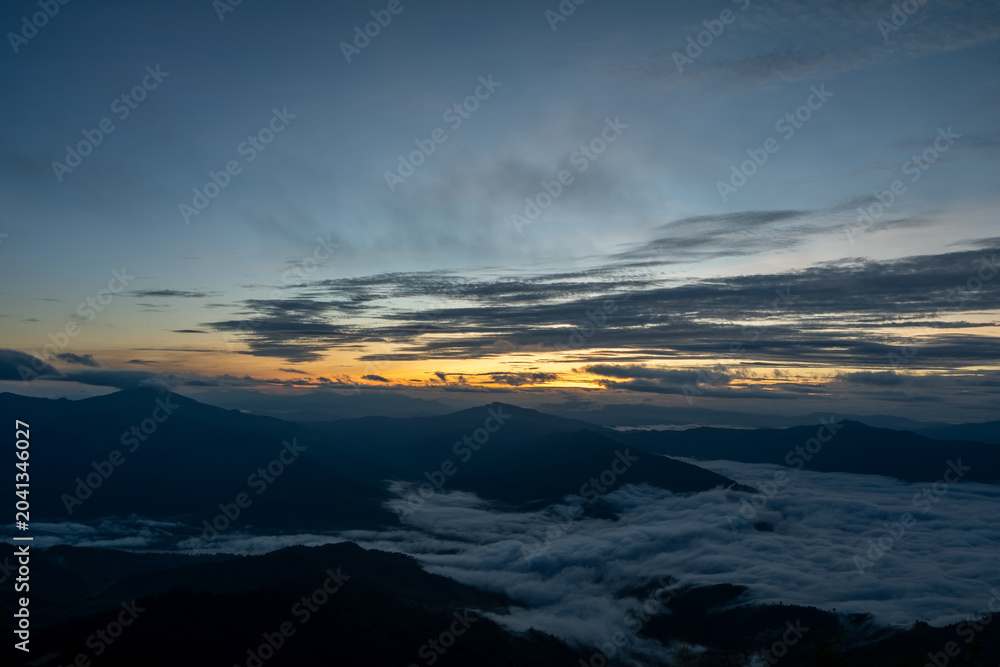 Fototapeta premium Early morning sunrise with mountain silhouette and clouds, calm natural landscape filled with morning mist.